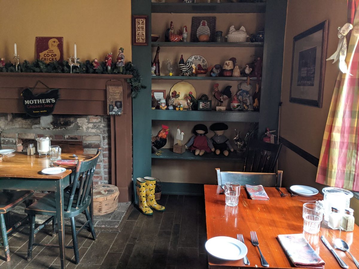 The Dining House set for dinner, with a fireplace mantel and folk-art shelves